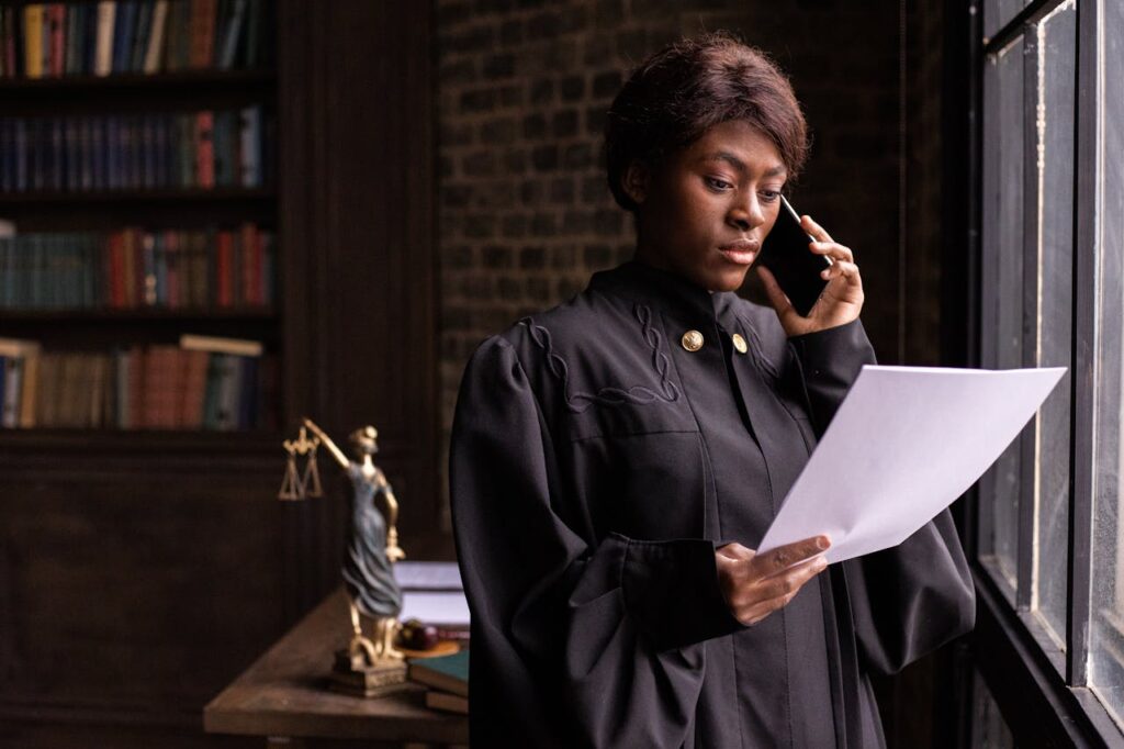pexels-photo-6077188 African American judge in robe, reading document and talking on phone by the office window.
